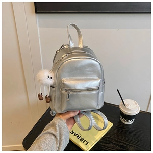 Detail of silver metallic mini backpack with fuzzy charm held in a lifestyle setting