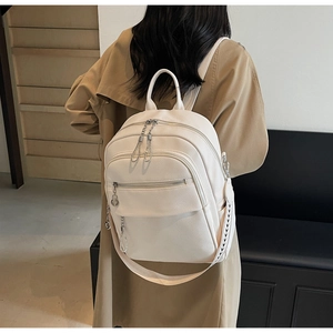 Side view of cream lychee texture leather backpack with multiple zip pockets and silver hardware