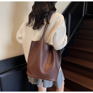 Detailed back view of a large brown tote bag with litchi grain texture on model