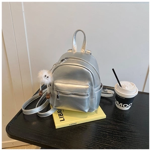 Detailed shot of a mini silver metallic backpack with a white plush charm on a table
