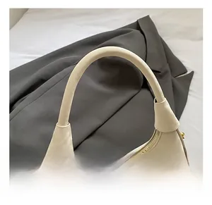 Détails de la poignée incurvée et des ferrures dorées sur un sac demi-lune couleur beige
