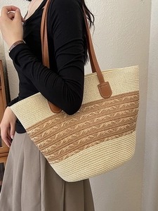 Large beige and brown woven beach tote bag with leather straps worn by a model