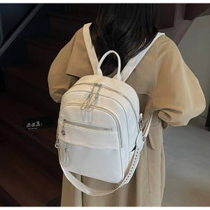 Close-up of white lychee leather backpack featuring metal chain charms and geometric strap