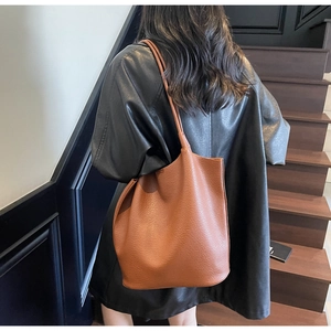 Brown leather tote bag with lychee texture shown on a model on wooden stairs