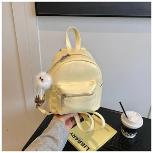 Close-up of mini yellow PU leather backpack with decorative fuzzy ball charm