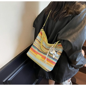Detalle del bolso tipo cubo de tejido a rayas con correas de cuero verde y colgante de estrella