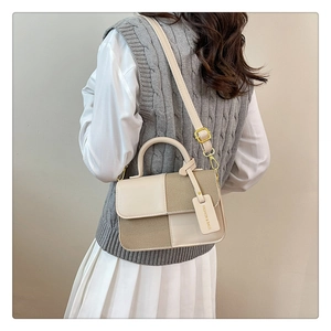Détail du sac bandoulière bicolore avec boucle en métal et étiquette en cuir