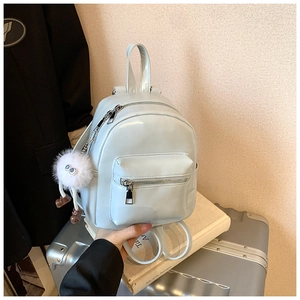 Close-up of light blue mini faux leather backpack with a plush monster charm on a suitcase