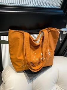 Orange canvas tote bag with floral embroidery and drawstring closure for women