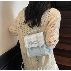 Detail of blue plaid backpack with bow decoration worn by a model on a wooden staircase