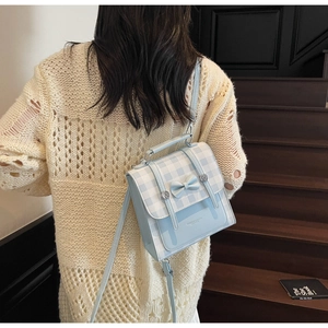 Detail of light blue plaid backpack with bow decor and silver studs on model back
