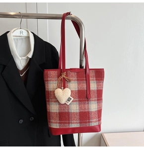 Détail d'un cabas en laine à carreaux rouge et beige avec un charme de cœur blanc