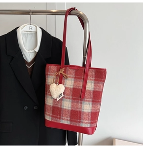 Détail du sac seau à carreaux rouge et beige avec un pendentif cœur en peluche blanc