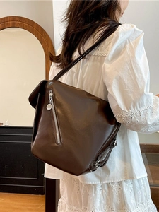 Brown soft leather tote bag with silver zipper detail, worn by a model in a warm setting