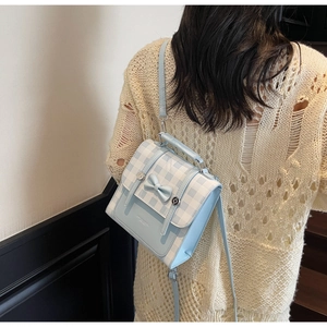 Detail of light blue plaid backpack featuring a 3D bow and silver magnetic clasp