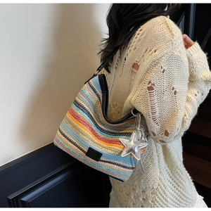 Detalle de bolso tipo cubo tejido a rayas de colores con correa de cuero negro en una modelo