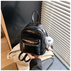 Close-up of black patent leather mini backpack with silver zippers and plush monster charm