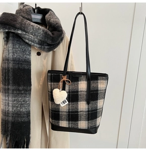 Détail du sac seau en laine à carreaux contrastés avec breloque cœur peluche et base en cuir