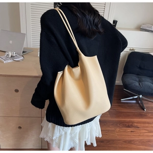 Minimalist beige tote bag in lychee pattern leather styled over woman's shoulder