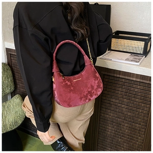 Détail d'un sac sous le bras en velours bordeaux avec chaîne dorée sur l'épaule