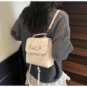 Detail of cream backpack featuring a bow-knot, gingham pattern flap and adjustable straps