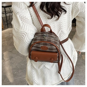 Detail of small brown plaid backpack with leather trim and adjustable straps on model
