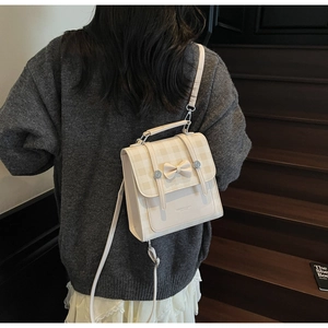 Rear view of model wearing a beige mini bow backpack with plaid flap and metal buckle