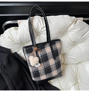 Détail du sac fourre-tout à carreaux avec lanières en cuir noir et breloque en peluche cœur