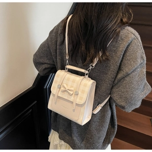 Close-up of a cream-colored mini backpack featuring a bow design and plaid flap detail