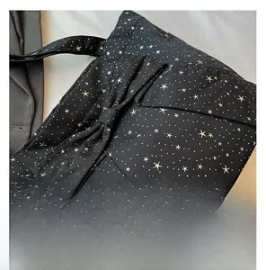 Detail of black canvas tote bag featuring white star patterns and large 3D decorative bow