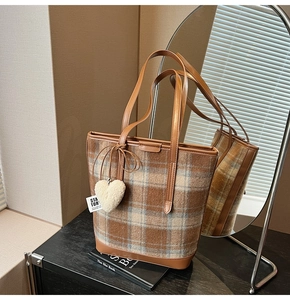 Detail of retro brown plaid tote bag with leather trim and white heart plush keychain