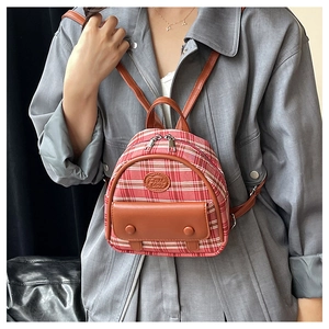 Detail of red plaid mini backpack with brown leather pocket and logo patch on model