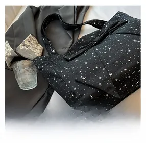 Detail of black canvas tote bag featuring white star pattern and wide shoulder strap