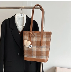 Détail du sac seau à carreaux avec breloque cœur et lanière en cuir sur fond blanc