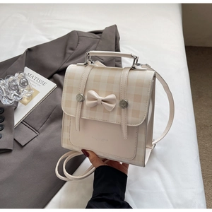 Detail of cream plaid mini backpack featuring a bow accent and silver buckles
