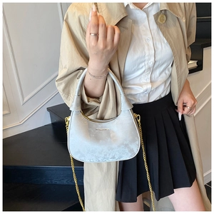 Détail du sac hobo argenté avec chaîne dorée porté par un mannequin en trench