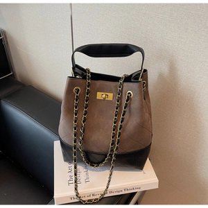 Detail of quilted bucket bag with gold square buckle and leather chain strap on books