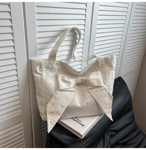 Detail of white canvas tote bag featuring a large bow and silver star print
