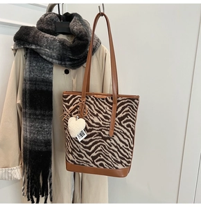 Détail du sac fourre-tout zébré en peluche avec base en cuir et breloque cœur