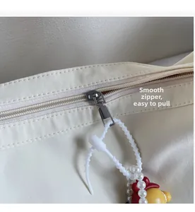 Detail of smooth metal zipper and decorative charm on cream checkered canvas bag