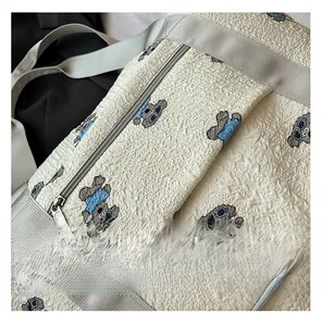 Close-up of quilted cream travel bag featuring a cute cartoon bear and silver zipper detail