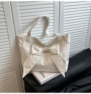 Detail of white canvas tote bag featuring silver star patterns and a large decorative bow