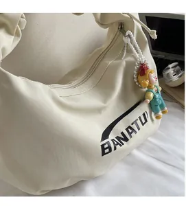 Detail of creamy white crescent bag with BANATU logo and cute cartoon charm detail
