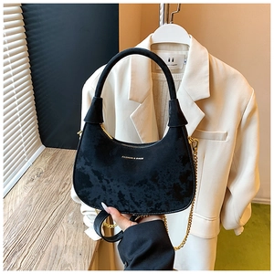Détail d'un sac hobo en velours noir avec chaîne dorée et inscription tendance