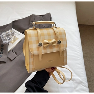Detail of yellow plaid backpack with elegant bow and metal buckle held by hand