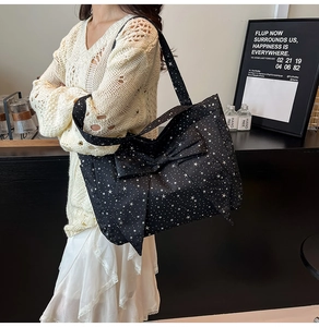 Detail of black canvas tote bag featuring white star prints and large decorative bow
