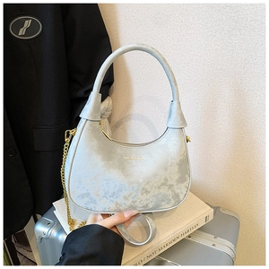 Détail d'un sac bandoulière bleu clair avec chaîne dorée sur des livres blancs