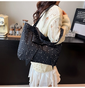 Detail of black tote bag with white star print and large decorative bow in a cafe setting