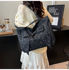 Detail of large black quilted tote bag featuring white star patterns and a bow decoration