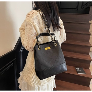Close-up of black quilted leather shoulder bag with gold chain and turn-lock detail